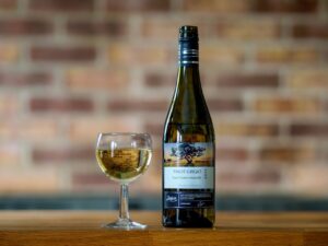Classic display of Pinot Grigio wine bottle and glass on a wooden table with brick background.