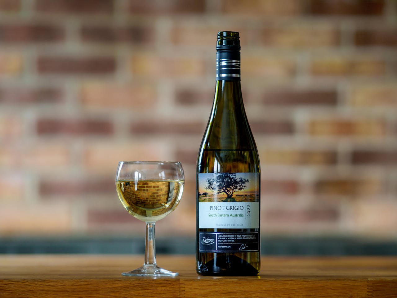 Classic display of Pinot Grigio wine bottle and glass on a wooden table with brick background.