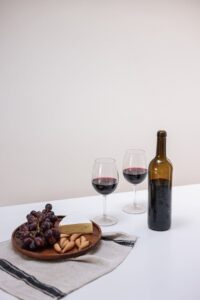 Elegant still life featuring red wine, cheese, and grapes on a table.