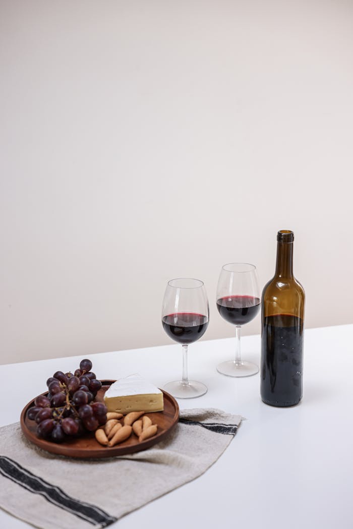 Elegant still life featuring red wine, cheese, and grapes on a table.